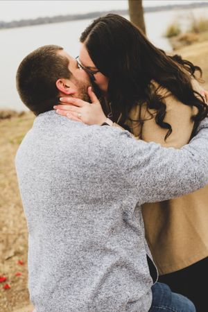 A romantic couple sharing a tender kiss outdoors with long dark hair flowing in the wind.