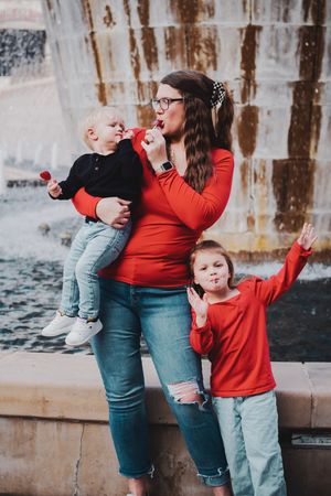 A family in matching red tops and jeans shares a candid moment together against a rustic wall backdrop.