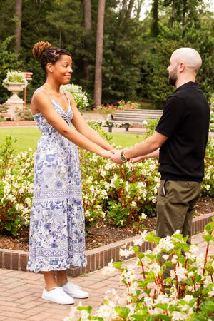 A couple shares a tender moment in a garden with blooming flowers and brick pathways.