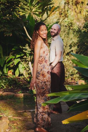 A couple shares romantic moments in a tropical garden setting with large green leaves and natural sunlight.