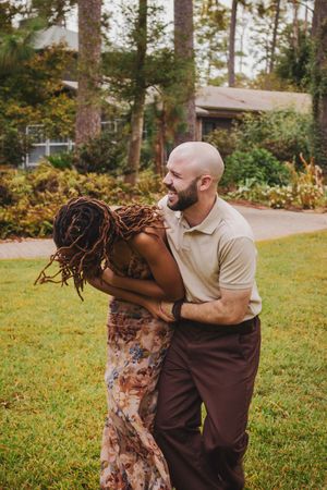A playful couple shares a joyful moment together on a grassy lawn surrounded by autumn trees.