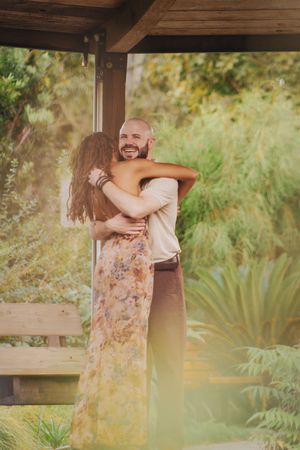 A couple embraces in a romantic moment outdoors surrounded by lush greenery and palm plants in a garden setting.