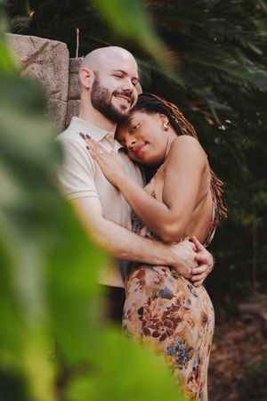 A loving couple embraces in a romantic outdoor setting with green foliage framing the intimate moment.