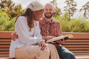 Couple sitting on wooden bench outdoors sharing tender moments in sunlit natural setting.