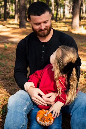 A parent and child share a tender autumn moment in the woods while holding a small decorative pumpkin.