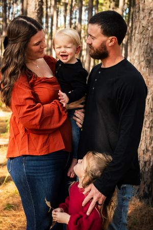 Candid family moments captured in a wooded setting with warm autumn lighting and coordinated red and black outfits.