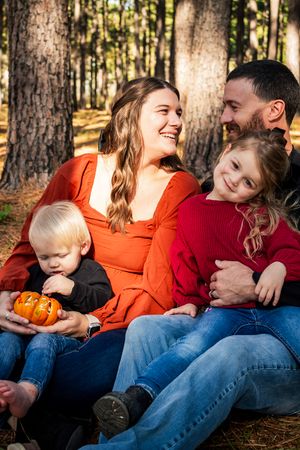 Intimate family portraits taken in a pine forest showing playful interactions and casual poses on fallen leaves.