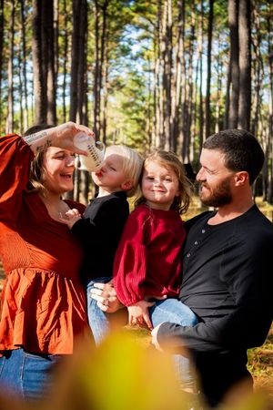 Couple sharing joyful laughter together while standing among tall pine trees in a sunlit forest setting.