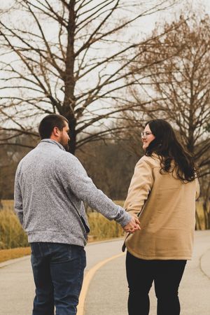A couple walking together on a path holding hands during a fall day with bare trees in the background.