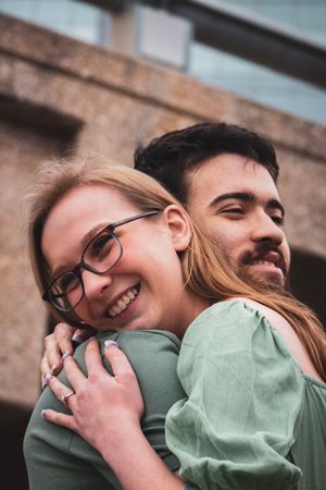A couple sharing a tender embrace and laughing together while wearing casual attire outdoors.