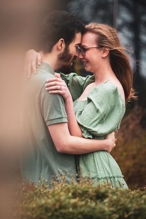 A romantic couple in mint green clothing embrace tenderly in a garden setting with soft bokeh lighting effects.