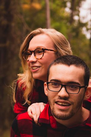 A couple wearing matching red plaid and glasses smile together in an autumn outdoor setting.