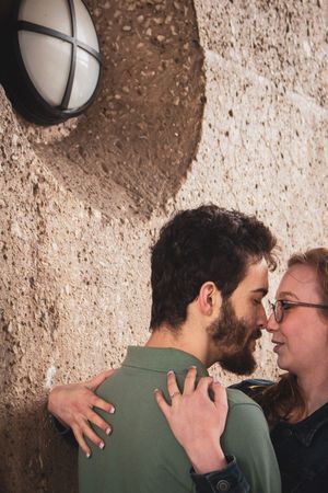 Two people in an intimate moment against a textured wall with dramatic lighting.
