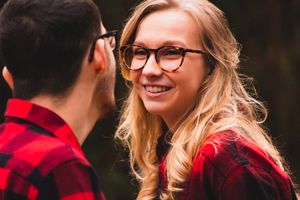 A couple in matching red plaid flannel shirts share romantic moments in a rustic outdoor setting during golden hour.