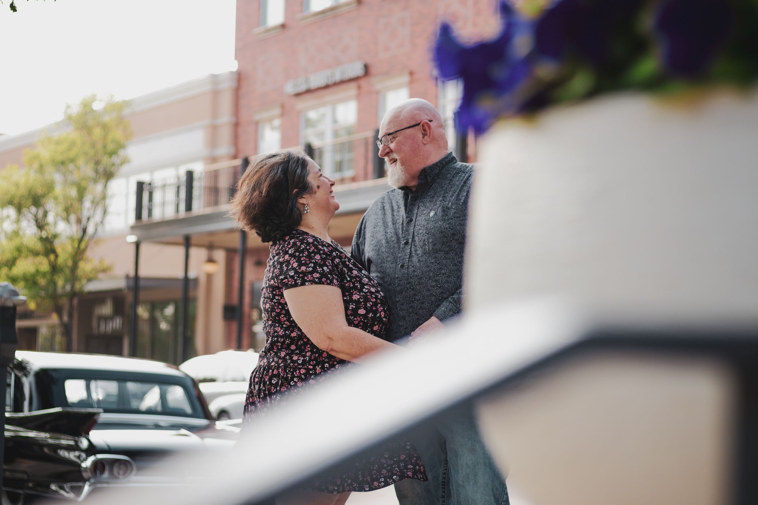 Elderly couple sharing a romantic moment on a downtown street, gazing lovingly at each other near a brick building.