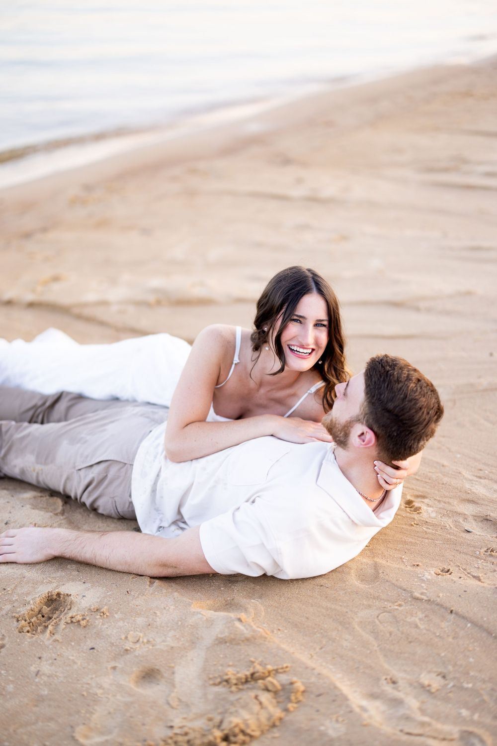 Romantic couple lying on sandy beach during sunset photo session.