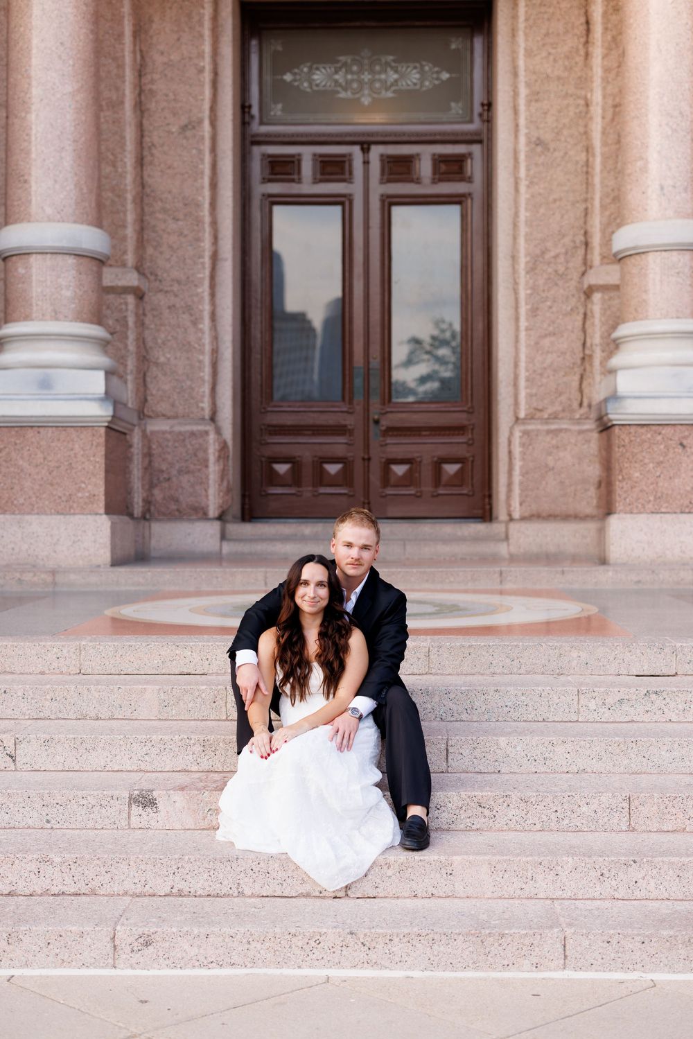A couple sits together on grand stone steps in front of an ornate doorway.