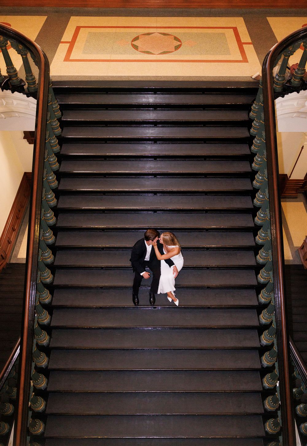 A couple shares a tender moment on a grand staircase with ornate railings.