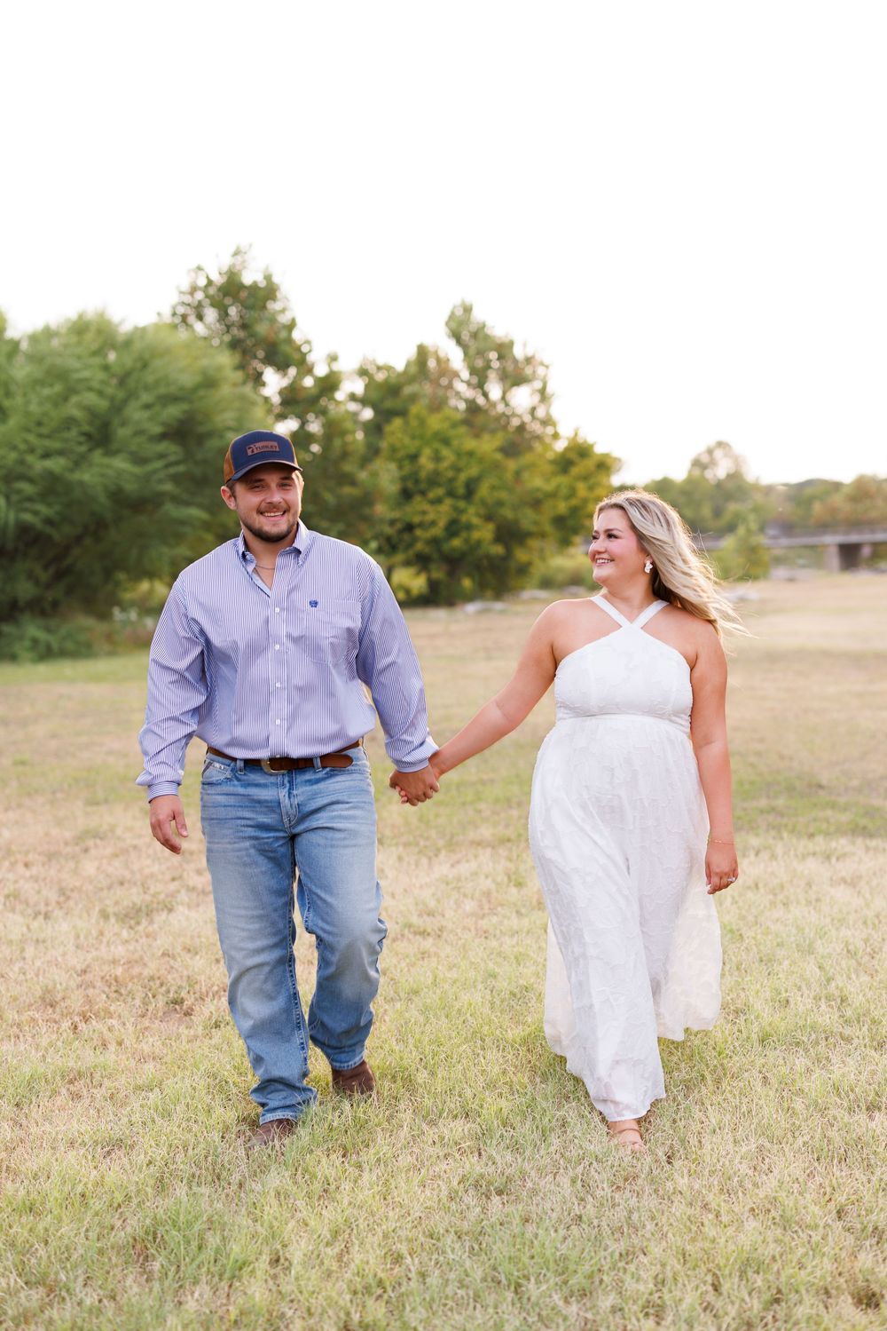A couple runs playfully through a grassy field during a countryside photoshoot.