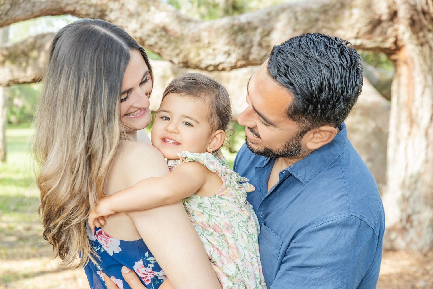 A family enjoys tender moments together outdoors during a professional photography session in a sunlit natural setting.