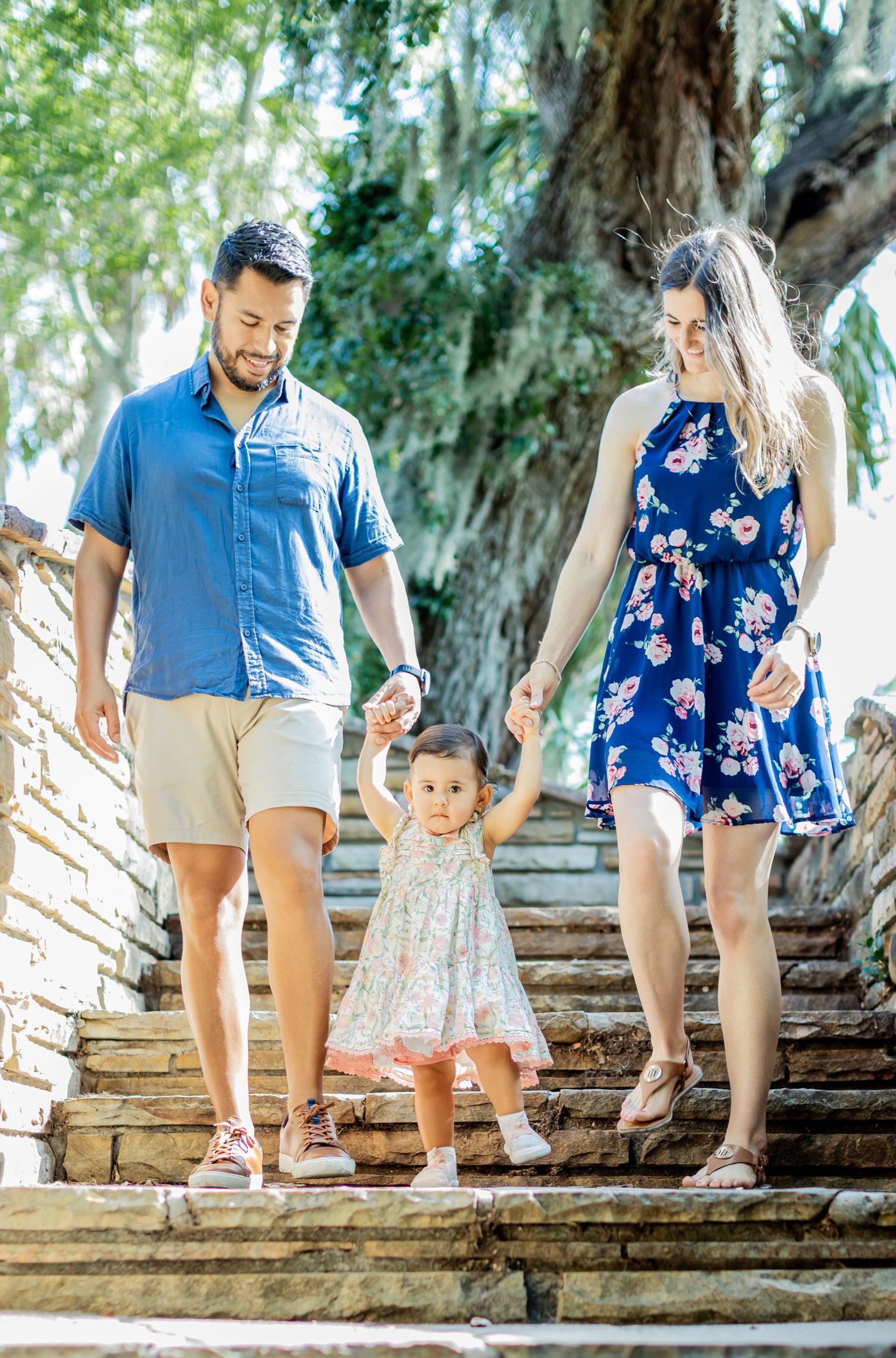 Family walking down rustic stone steps surrounded by lush greenery on a sunny day.