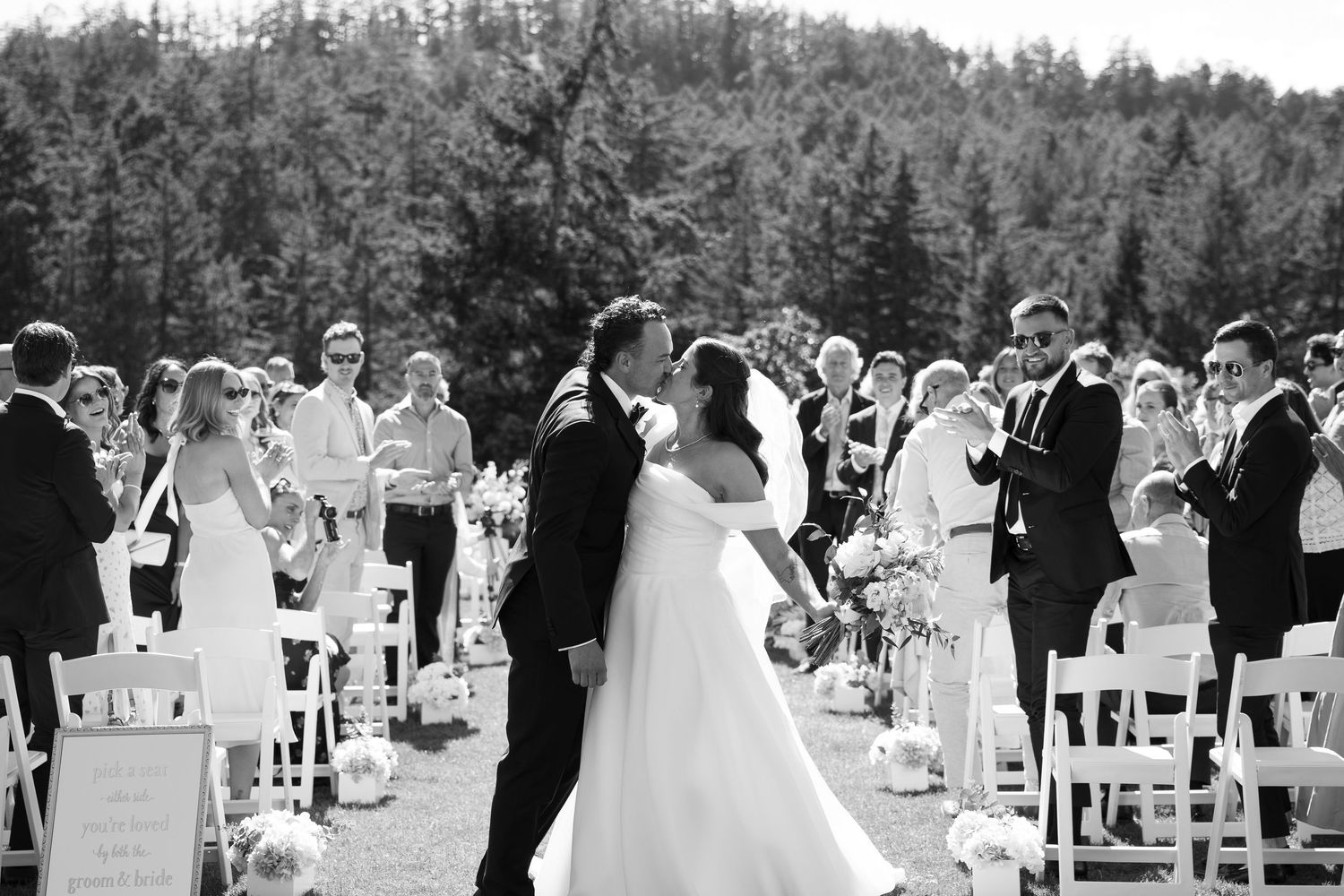 Bride and groom share a tender moment outside a rustic wooden barn venue in black and white photo.