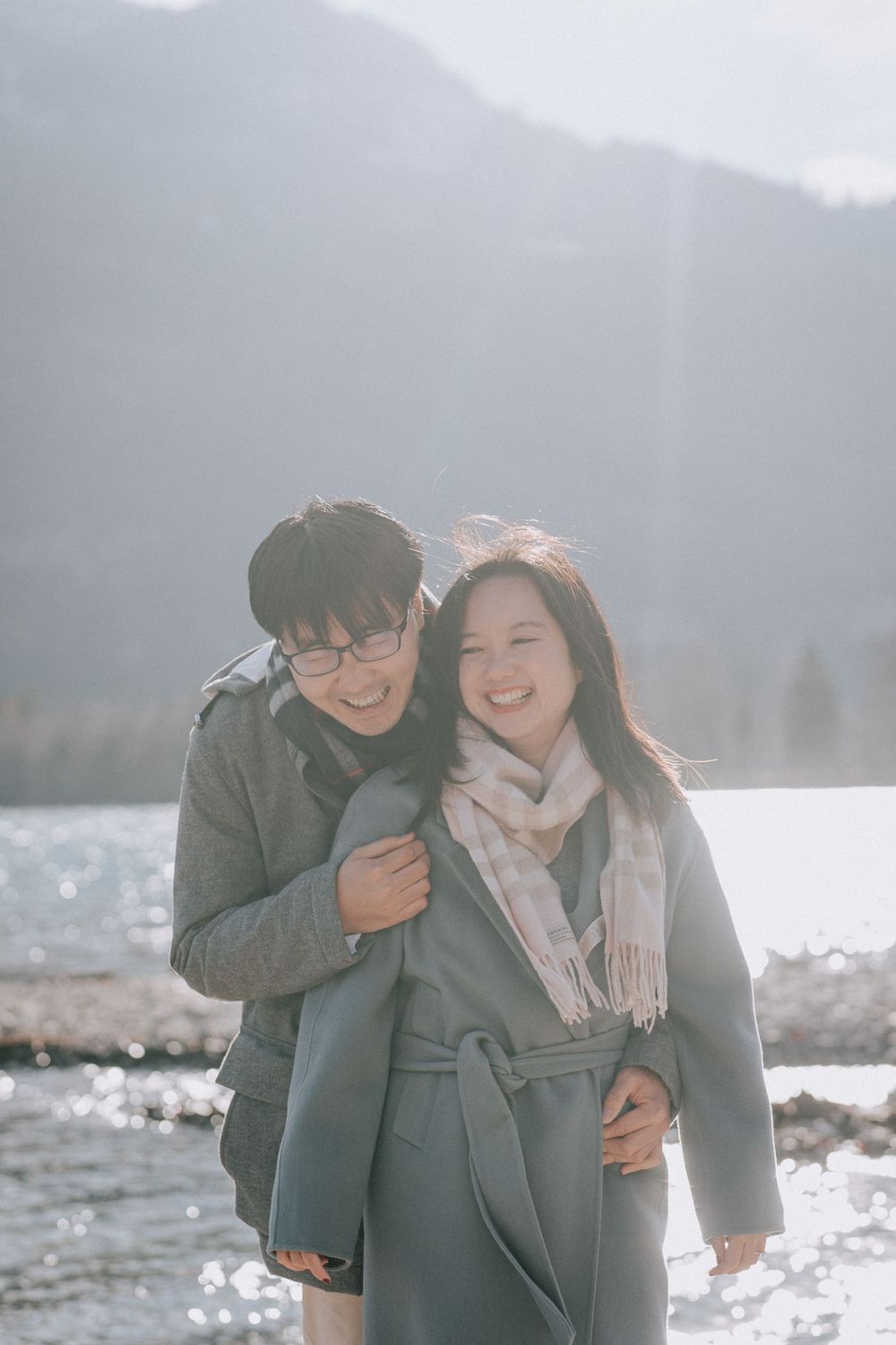 Couple laughing together on a winter day by a mountain lake.