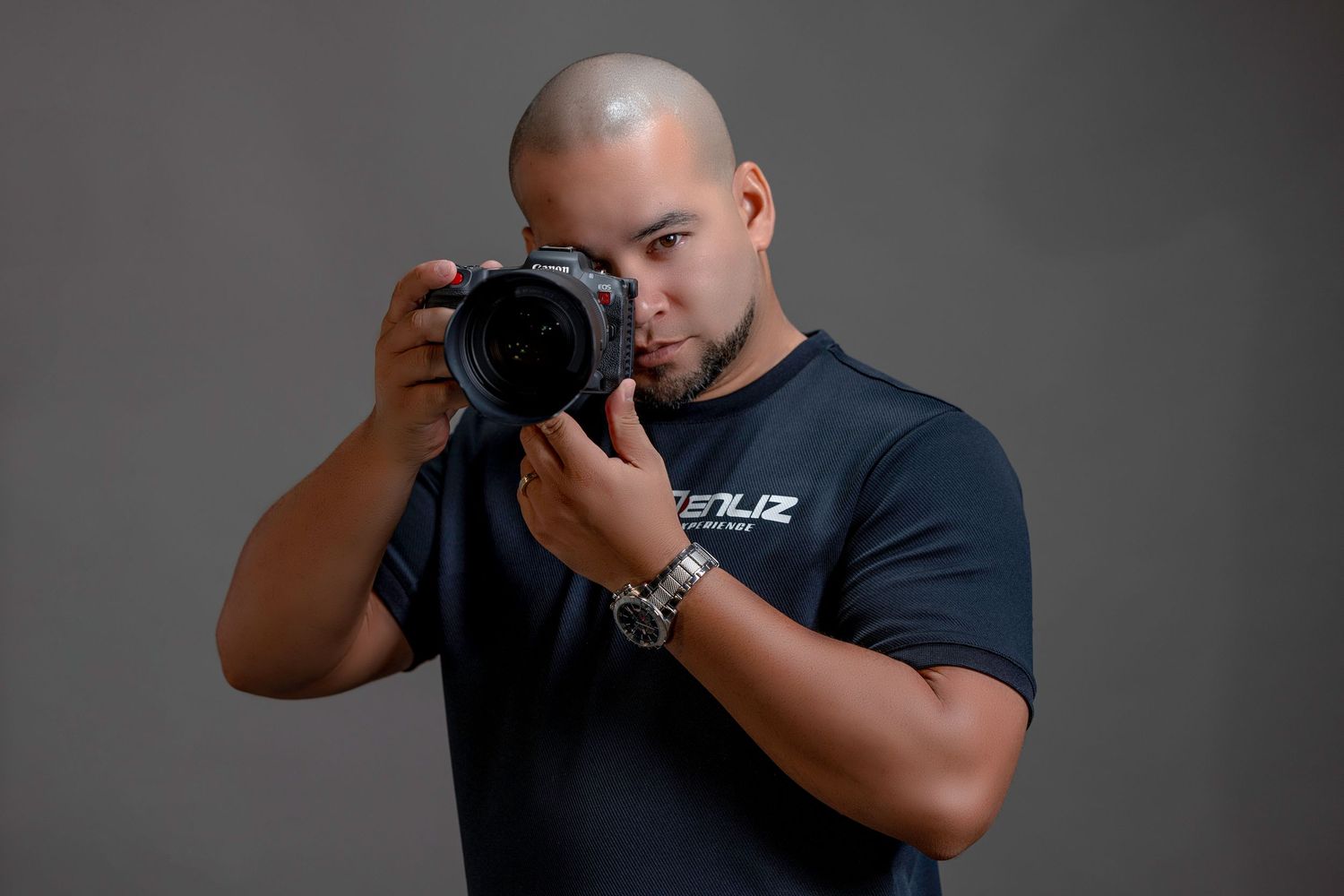 Bald male photographer holding a professional camera in a studio setting.