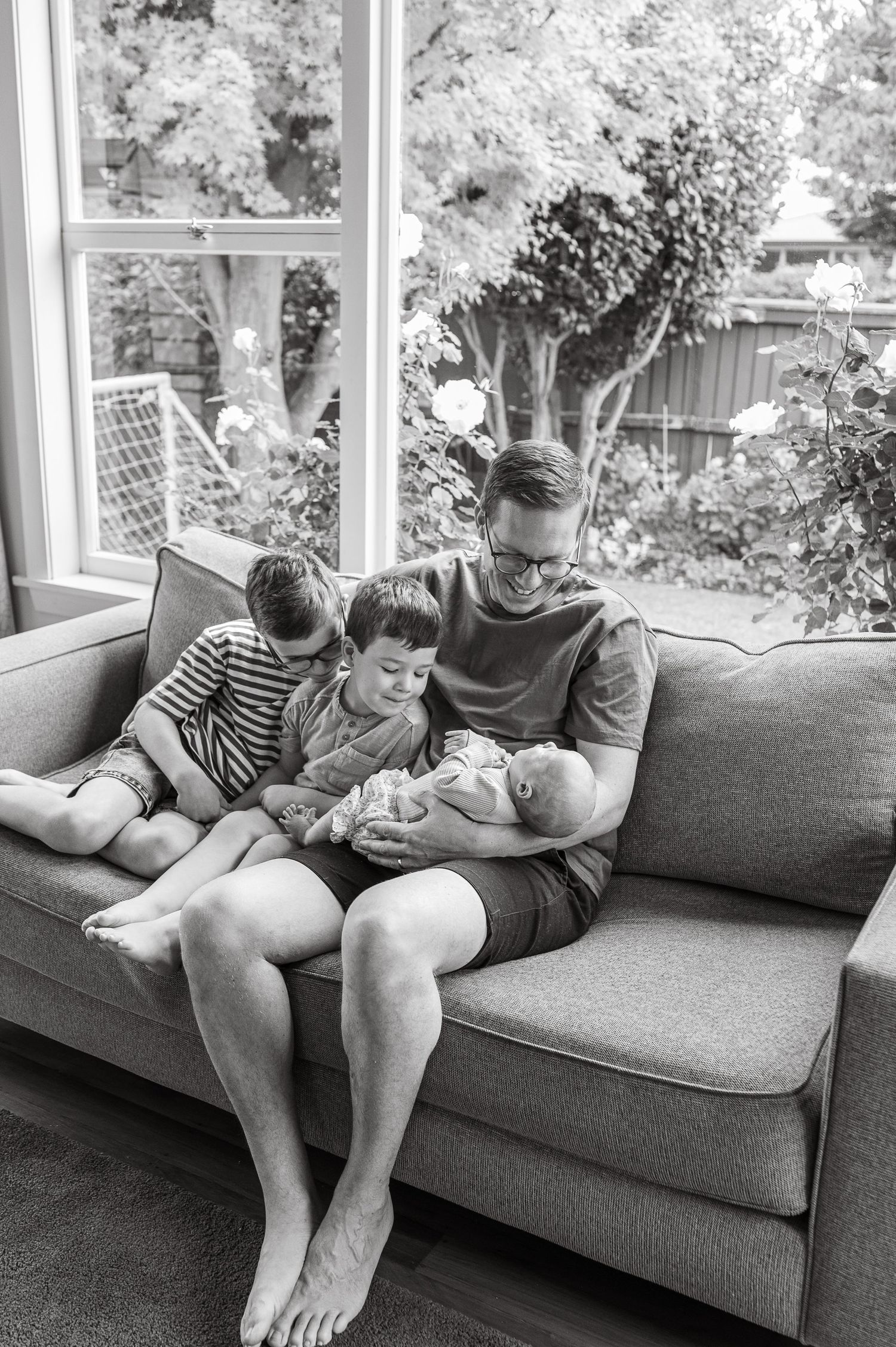 A black and white photo of a cozy family scene on a sofa by a bright window.