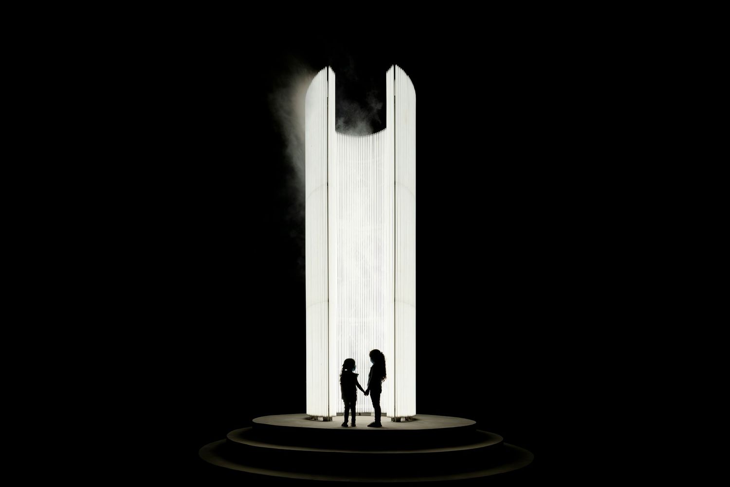 Two silhouetted figures standing in dramatic light between tall white pillars with dark shadows surrounding them.
