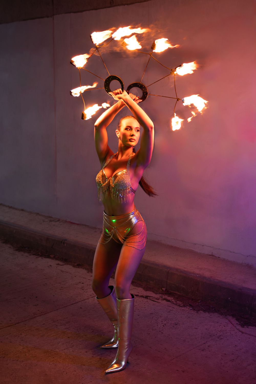 A performer in a sparkly costume dances with a flaming prop featuring multiple fire points in a dramatic nighttime shot.