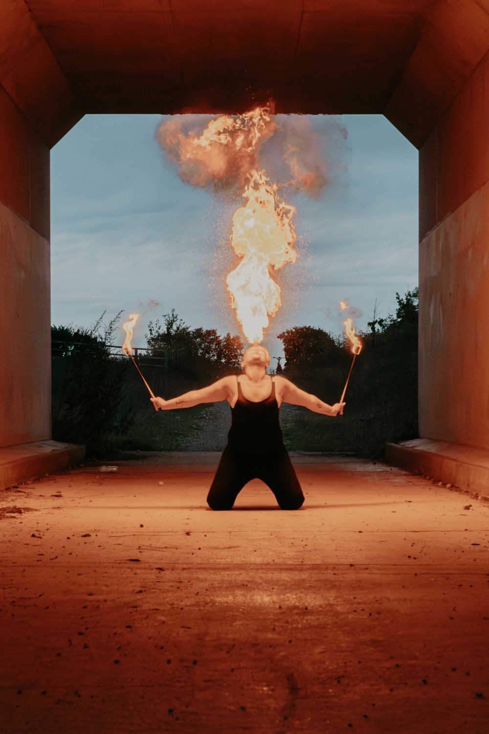 Fire performer creates dramatic effect with flame elements in concrete tunnel.