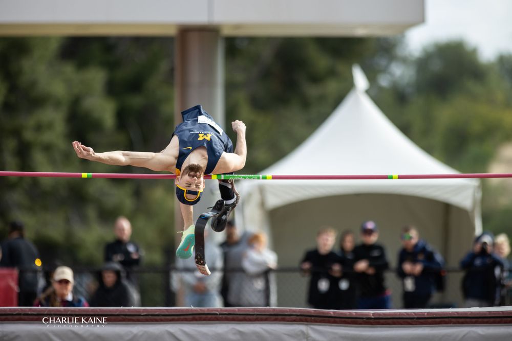 High jumper arches backwards over bar during competition with white tent in background.
