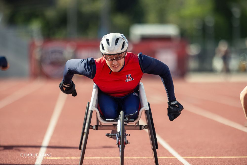 Wheelchair racer competes in navy and red uniform on track.