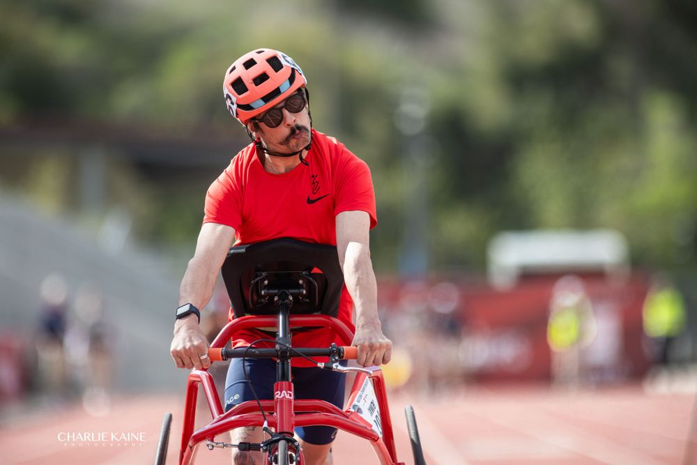 Wheelchair athlete in red racing on outdoor track during competition.