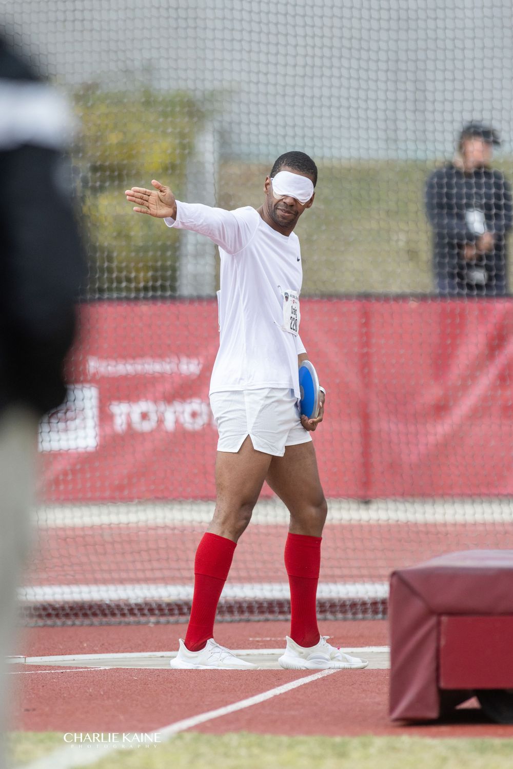 Athlete in white uniform performs shot put throwing motion on red track.