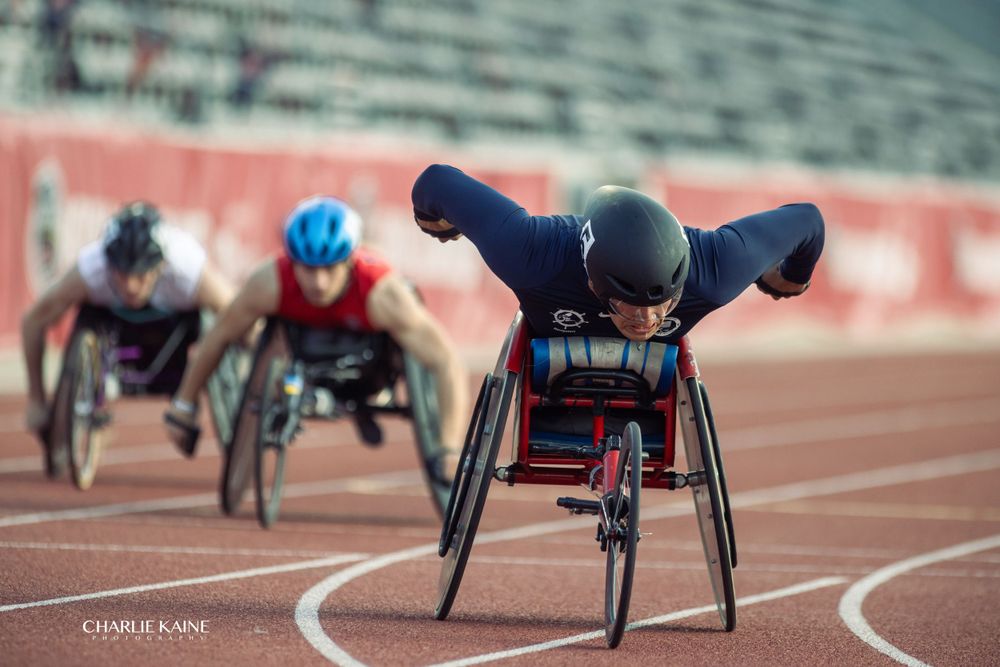 Paralympic athletes race in wheelchairs around curved track.