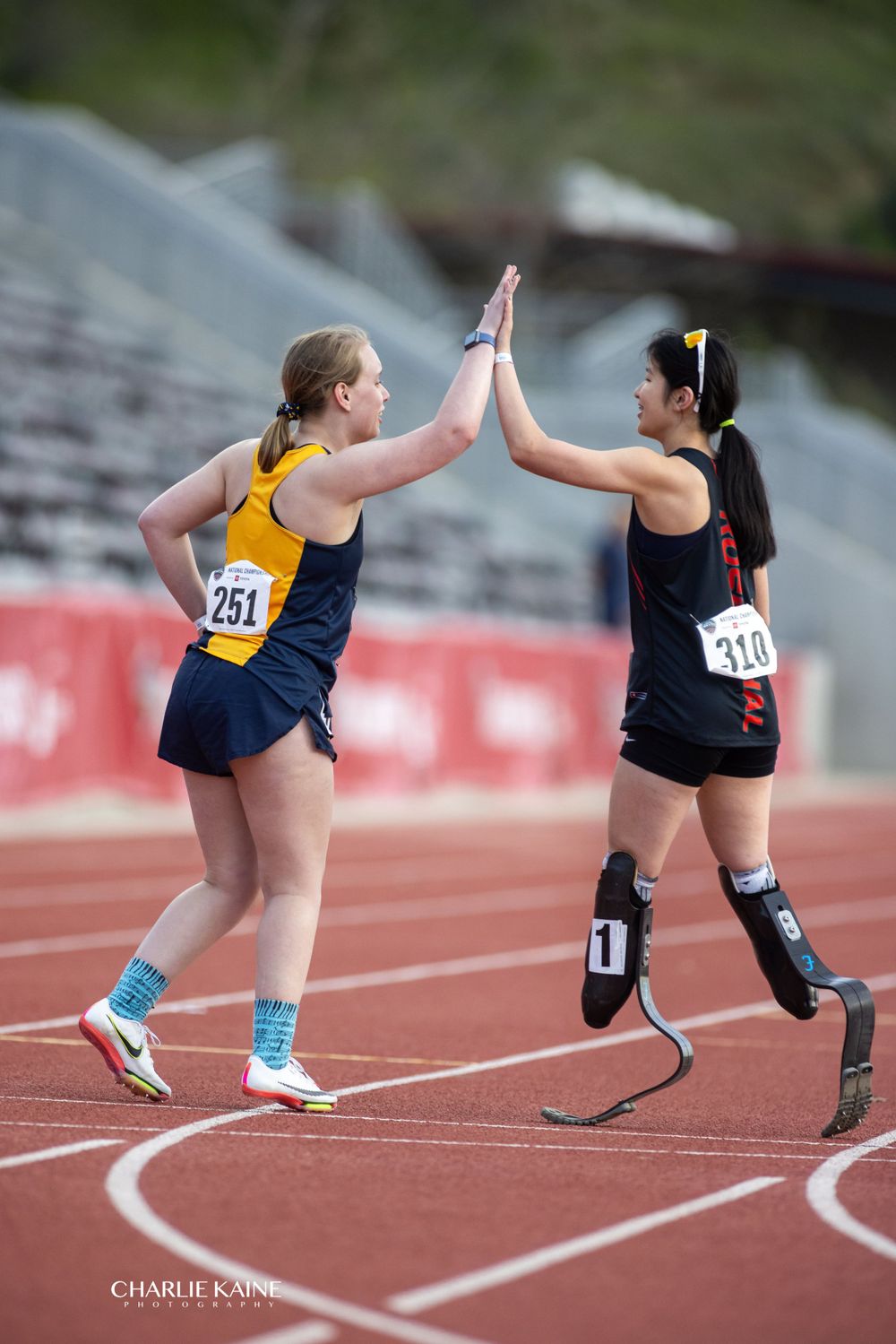 Athletes with prosthetic legs preparing to race on red track.
