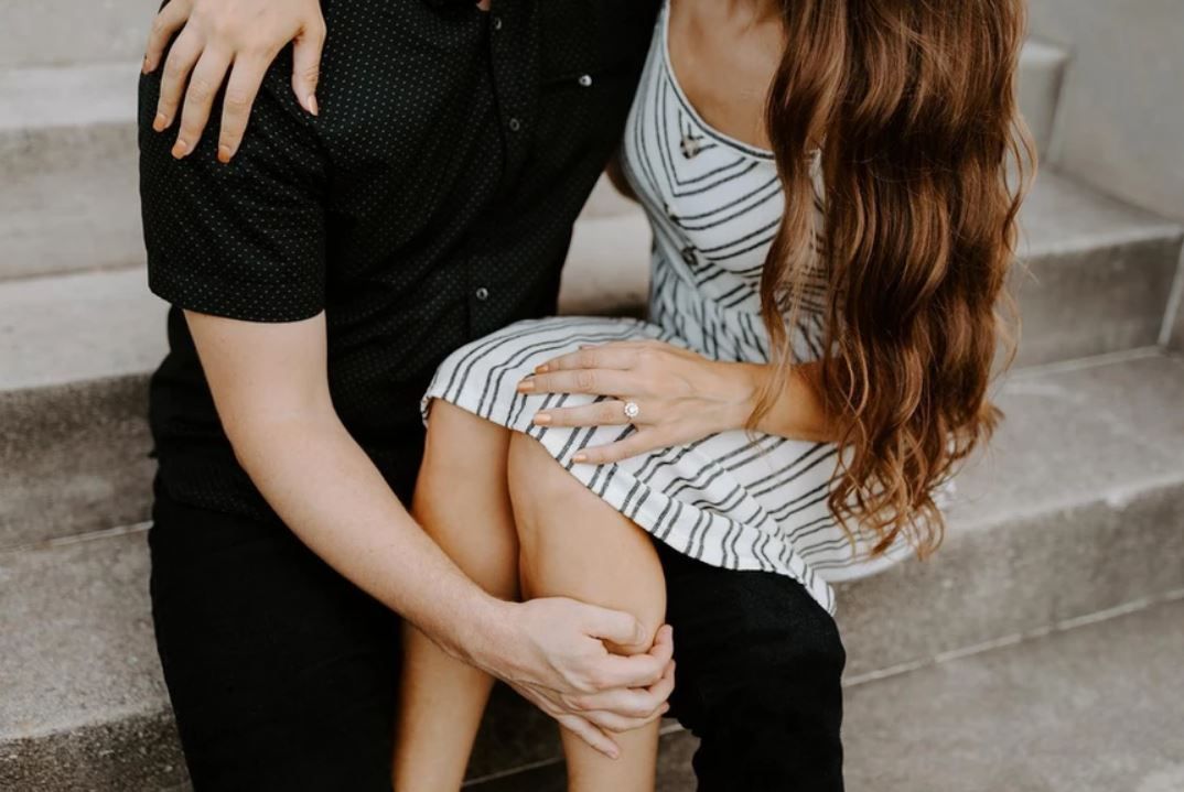 Intimate photo of two people sitting on gray steps, one wearing a black outfit and other in a striped dress.