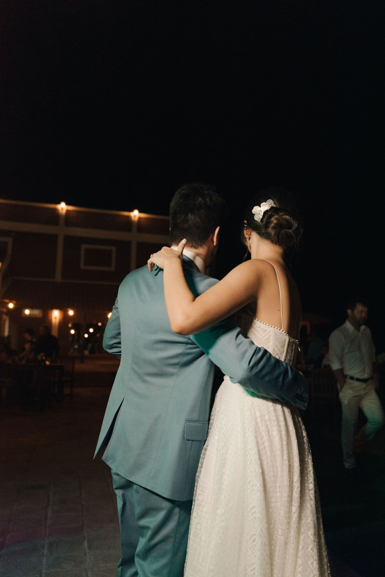 A couple embraces during an intimate dance moment under string lights at night.