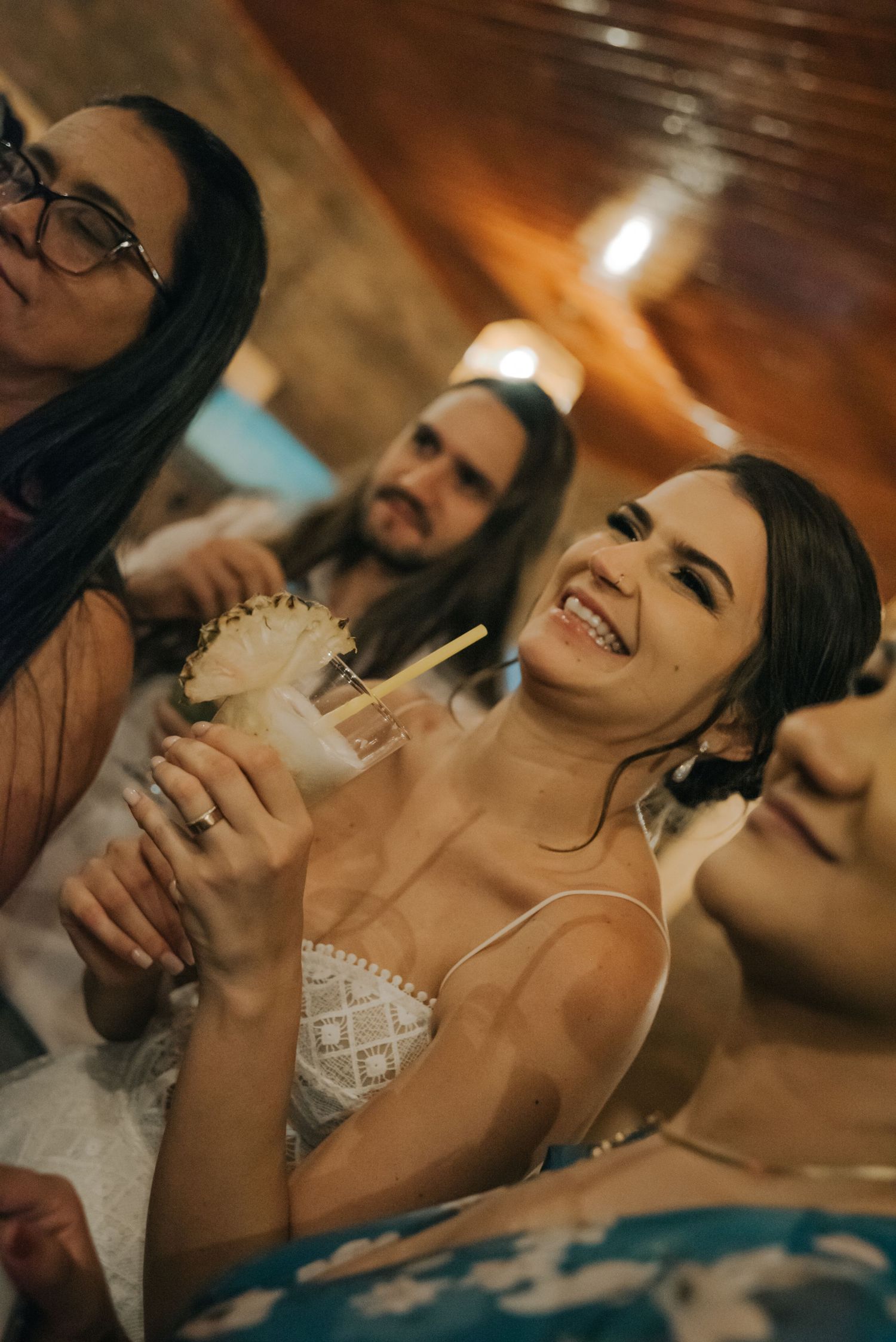 Wedding guests enjoy drinks and laughter at an indoor reception with warm lighting.