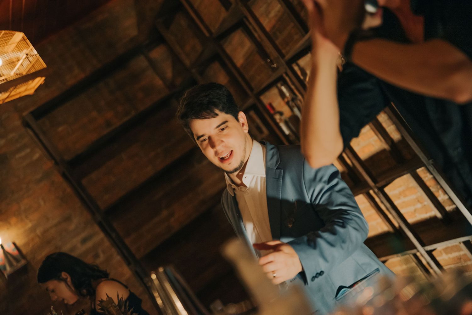 Energetic dancing at a wedding reception under wooden beams and pendant lights.
