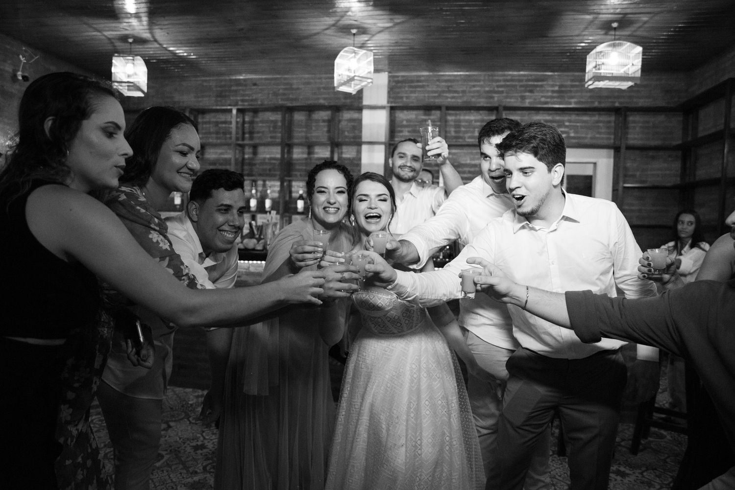 Black and white photo of joyful wedding celebration with guests dancing in rustic venue.