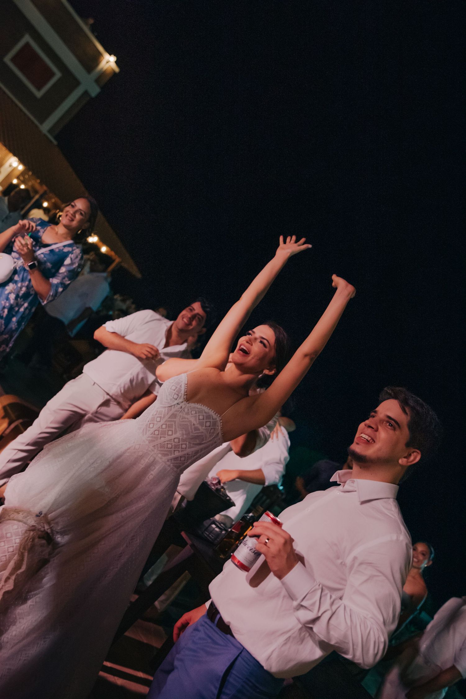 Energetic wedding celebration with bride and guests dancing under night sky.