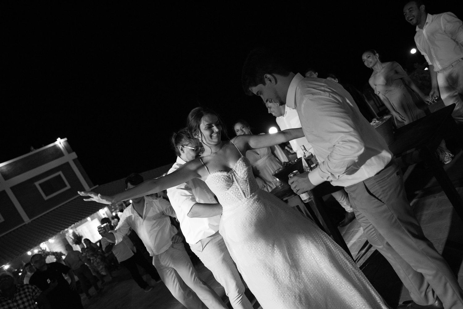 Black and white shot of wedding party dancing in line formation outdoors.