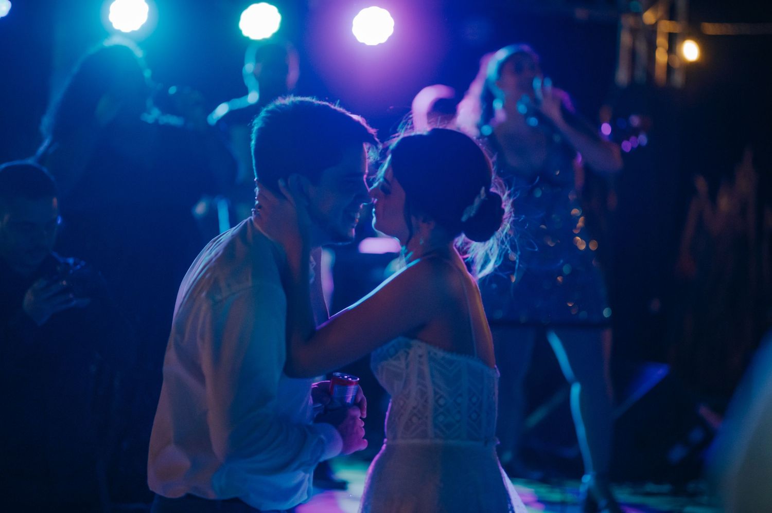 A couple shares an intimate dance moment under blue and purple stage lights at a nighttime celebration.