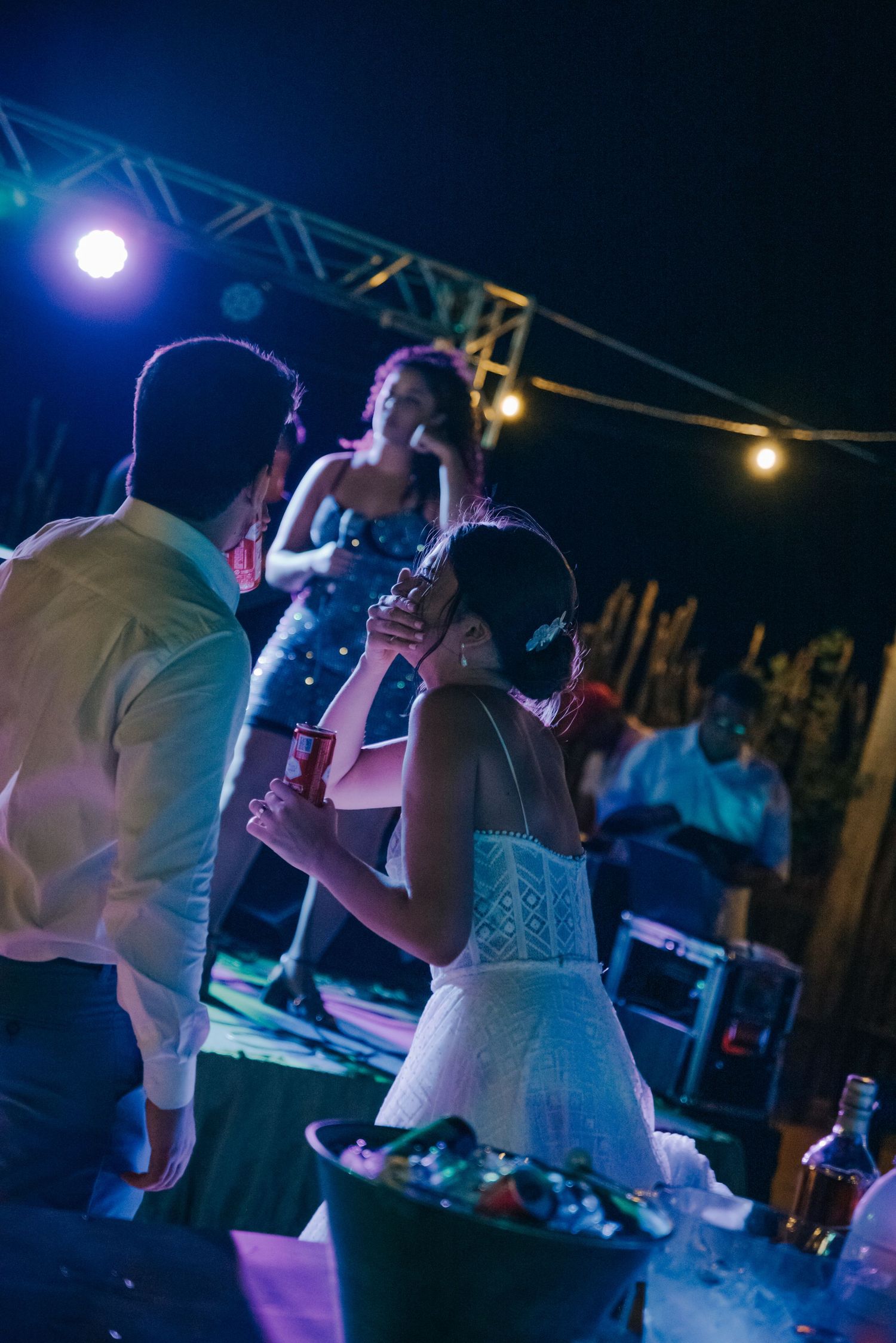 People dancing and celebrating at a nighttime event with colorful stage lighting overhead.