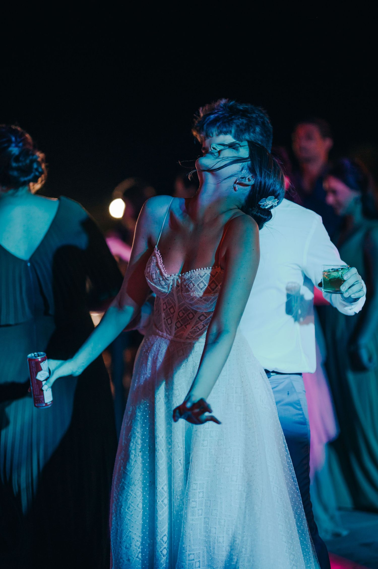A person in a white dress dances under moody blue lighting at a nighttime celebration.