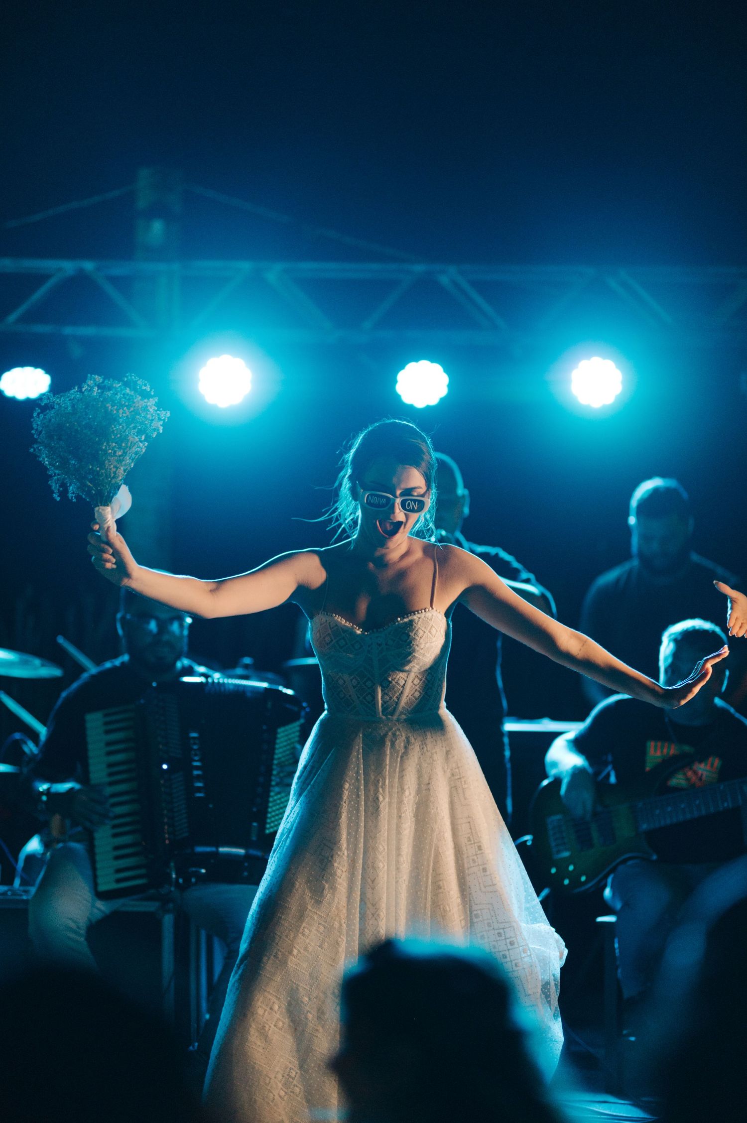 A dancer in a white gown performs under blue stage lighting with a band playing behind.