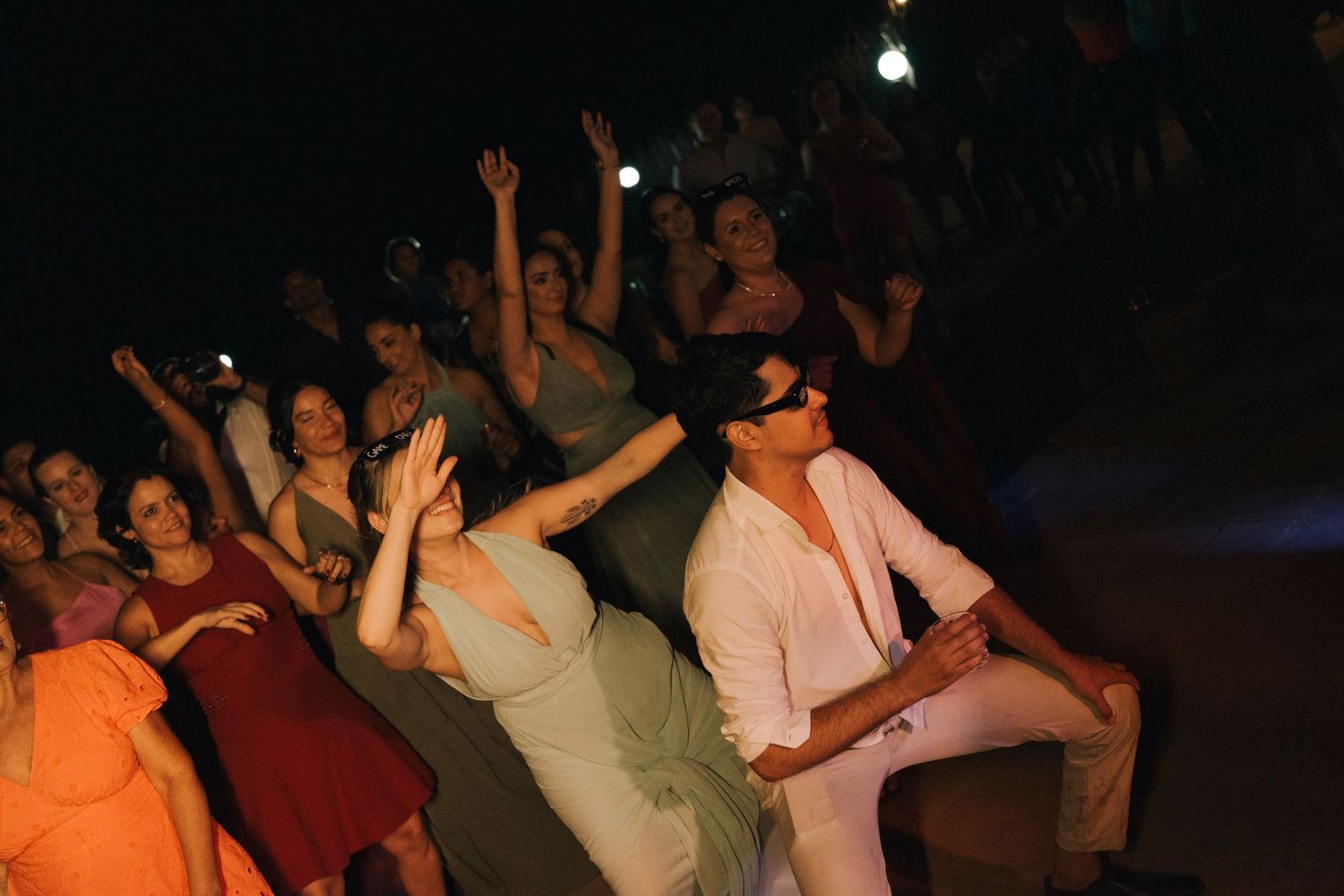Energetic wedding reception dance floor with guests dancing and celebrating under stage lights.